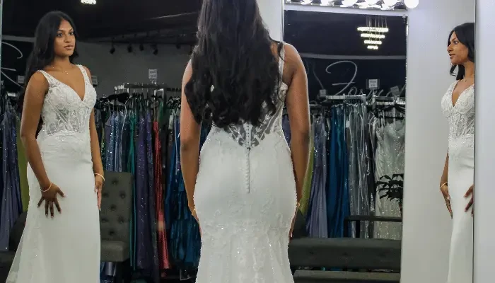 Bride in a fitted white lace wedding dress viewing the gown from the front and back in a bridal boutique.