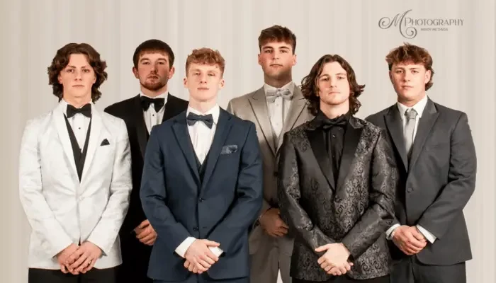 Six men posing together in different formal suits and tuxedos, including black, white, navy, gray, and patterned styles.