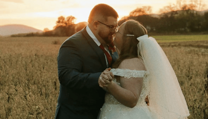 Bride and groom sharing a dance at sunset in an open field, featuring the groom in a dark wedding suit and the bride in an off-the-shoulder wedding gown.
