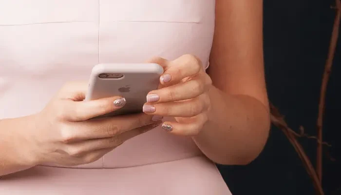 Woman in a light pink dress using a smartphone, with her hands and manicured nails visible.