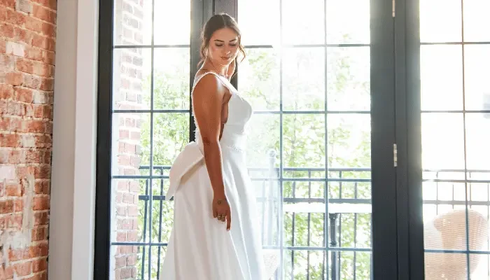 1. Bride in a simple white wedding dress standing by a large window.