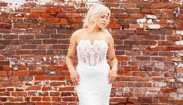 Bride in a strapless lace wedding dress posing in front of a brick wall.