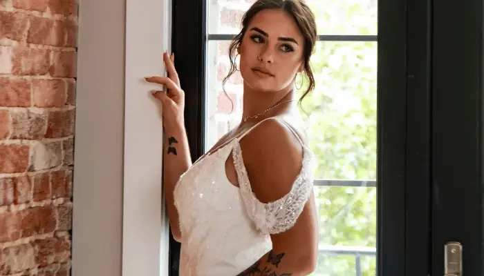 Bride in a white wedding dress standing by a window in a bridal boutique.