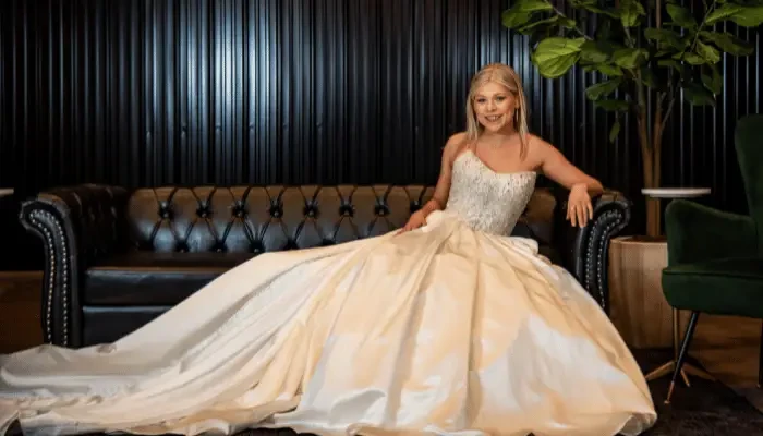 Bride in a full-skirted wedding gown sitting on a leather sofa.