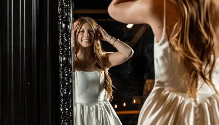 Smiling bride admiring her reflection in a mirror while wearing a white wedding dress.