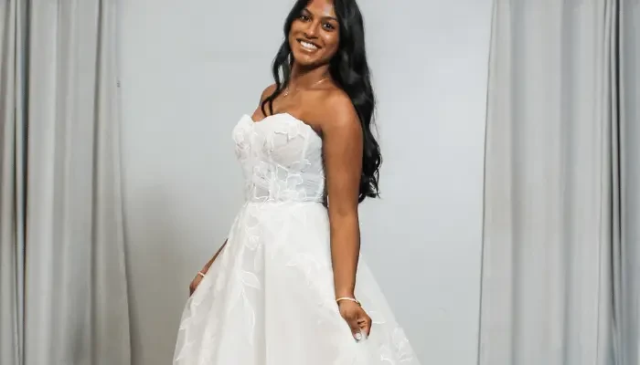 1. Smiling bride posing in a strapless white wedding dress with floral detailing in a bridal boutique.