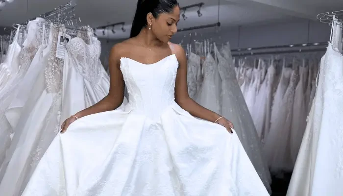 Bride holding out the full skirt of a white embroidered wedding dress while shopping in a bridal boutique.
