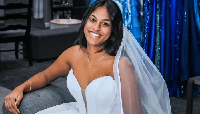 Smiling bride wearing a white strapless wedding dress and veil while sitting in a bridal boutique.