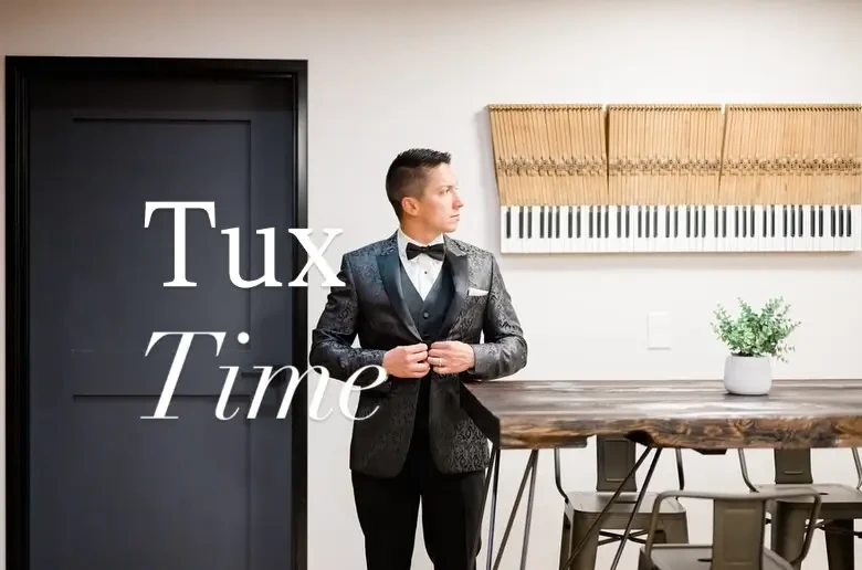 Man in a stylish tuxedo adjusting his bowtie in a modern, minimalist setting.