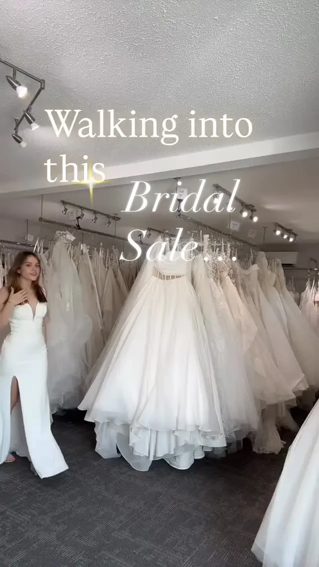 Bridal sale preview with a smiling woman standing amidst rows of beautiful wedding gowns.