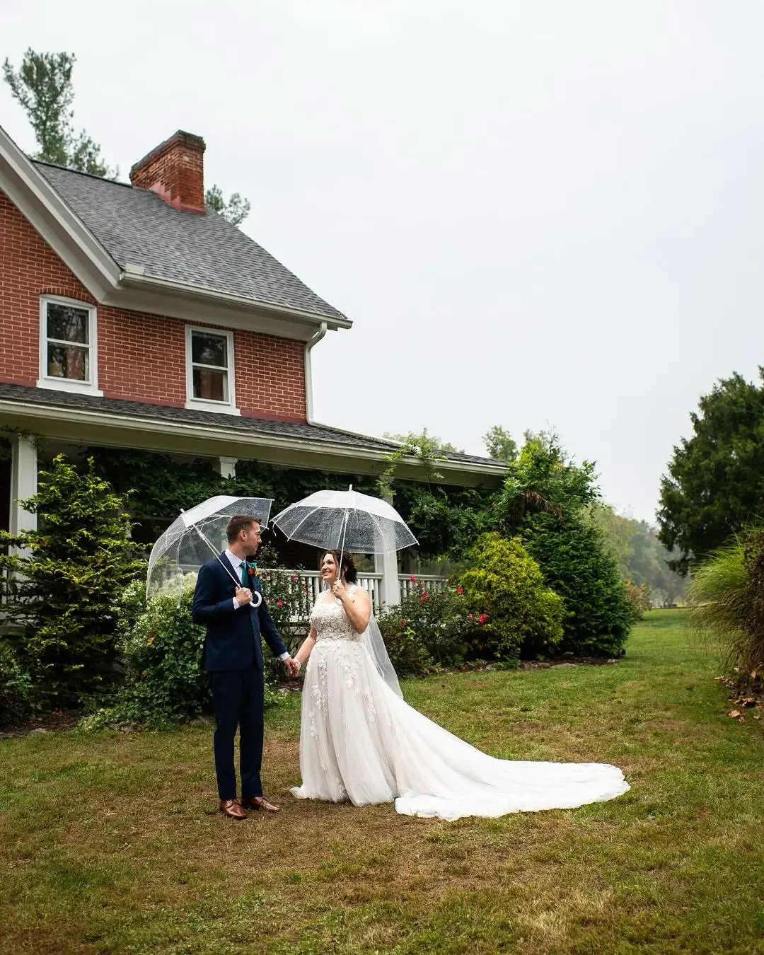 Bride and groom holding clear umbrellas in a romantic outdoor setting, with the bride's gown